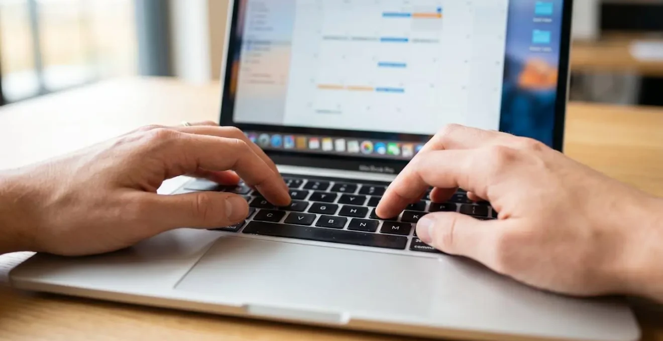 Primo piano ravvicinato di mani che digitano su una tastiera moderna di laptop con schermo sfocato sullo sfondo